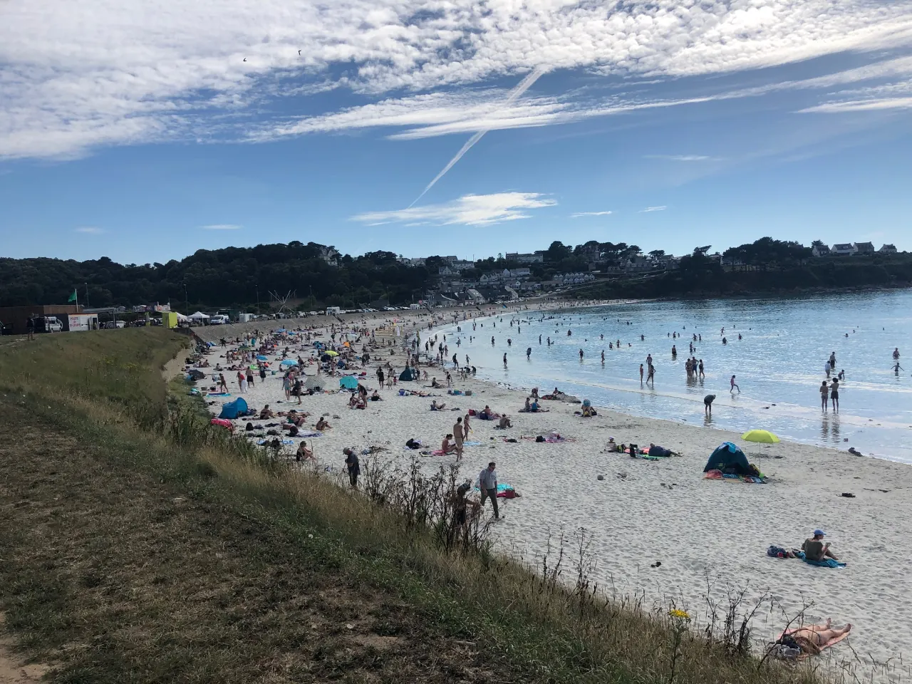 La plage de Trestel un jour d'été, vue depuis le talus qui la borde : baigneurs, parasols et longue courbe de sable fin.