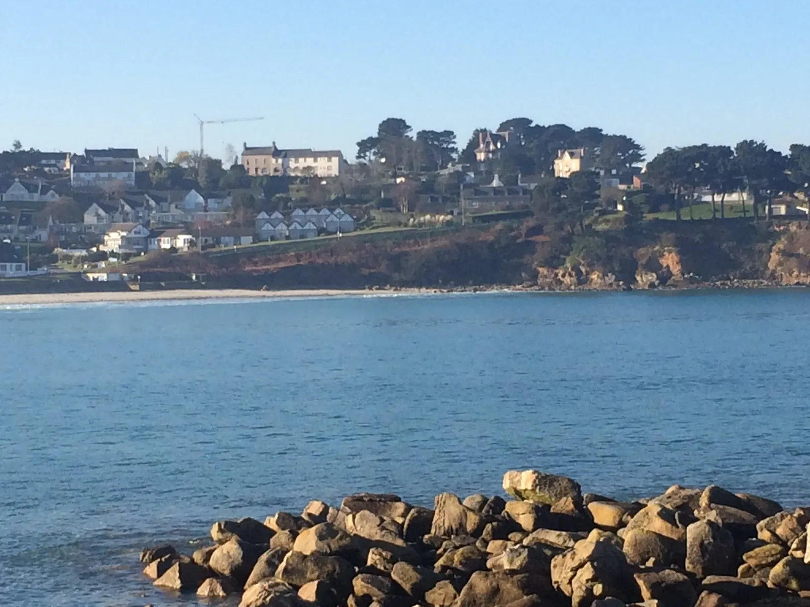 Trestel bay on a sunny winter's day: calm sea, rocks in the foreground and the houses of Trévou-Tréguignec on the hillside.